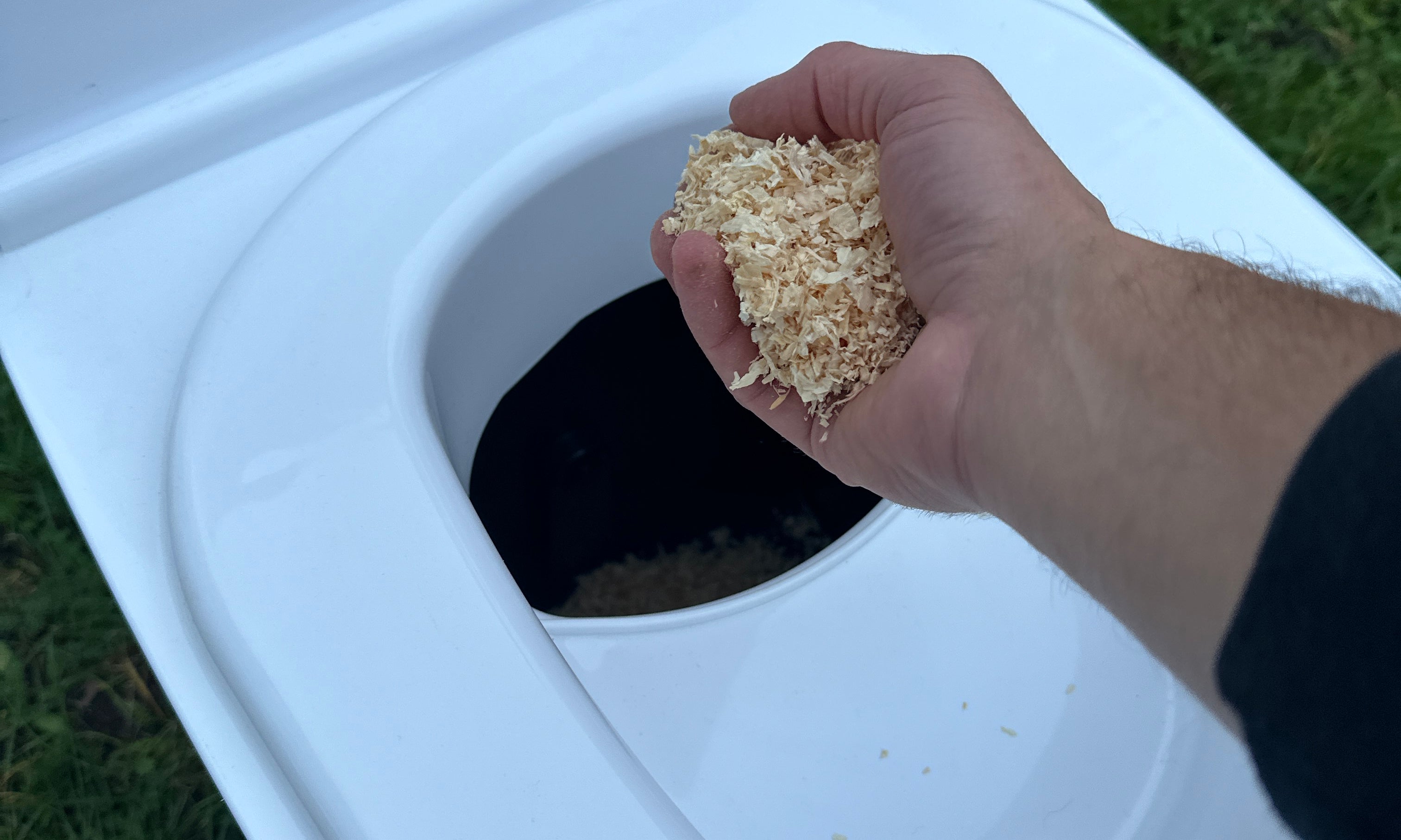 The laying method shown with Cuddy Lite. A hand is shown layering sawdust into the solids section of Cuddy Lite. 