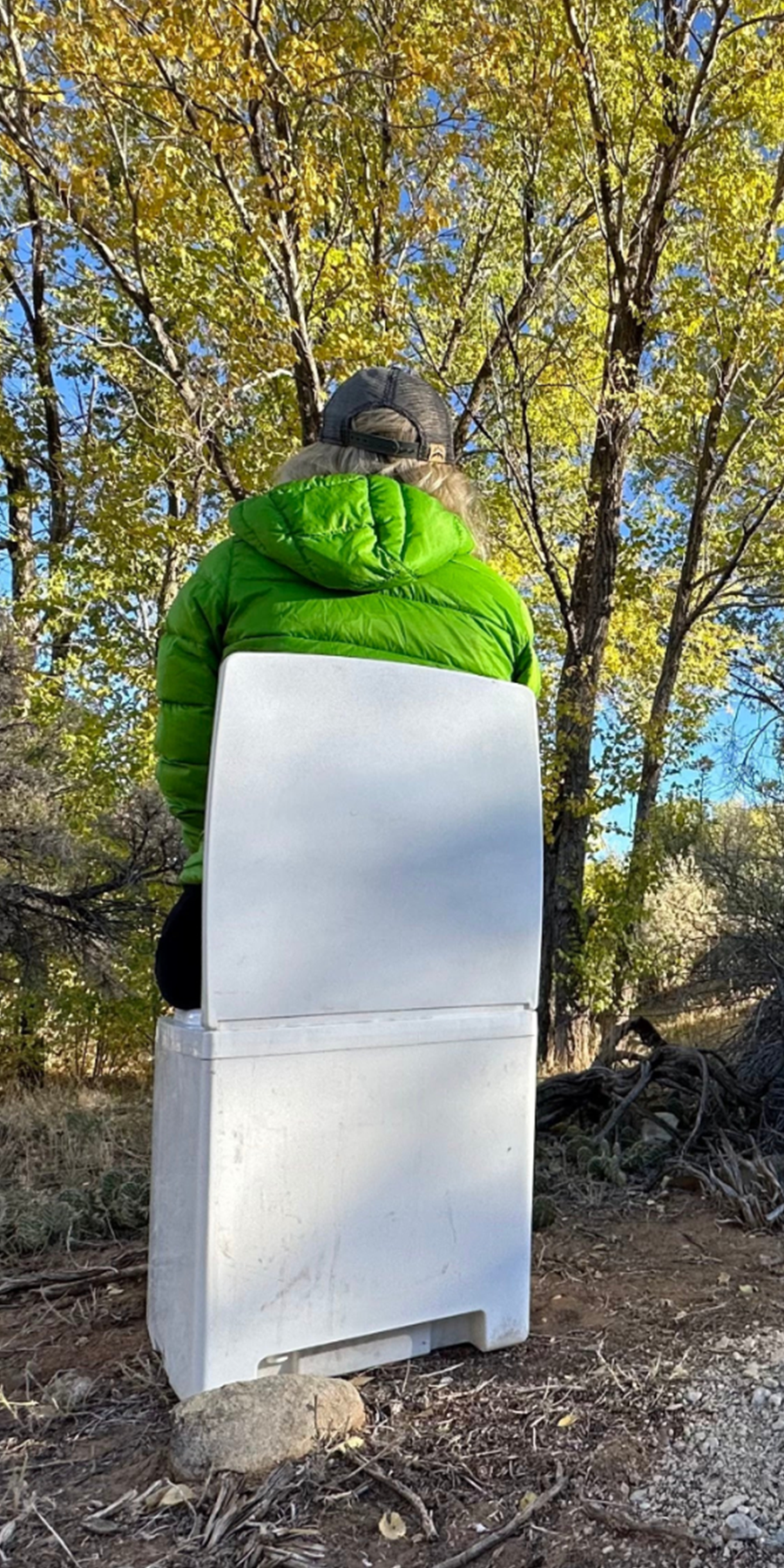 Person in a green jacket sitting on the Cuddy Composting Toilet in a forest setting